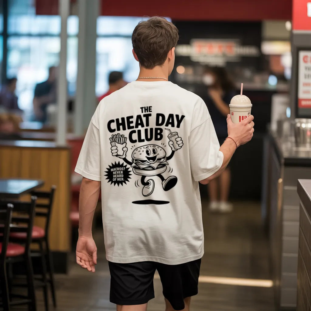 The Cheat Day Club (Backprint) Oversized T-Shirt White – Steel Spirit, worn by male model holding milkshake in fast-food restaurant